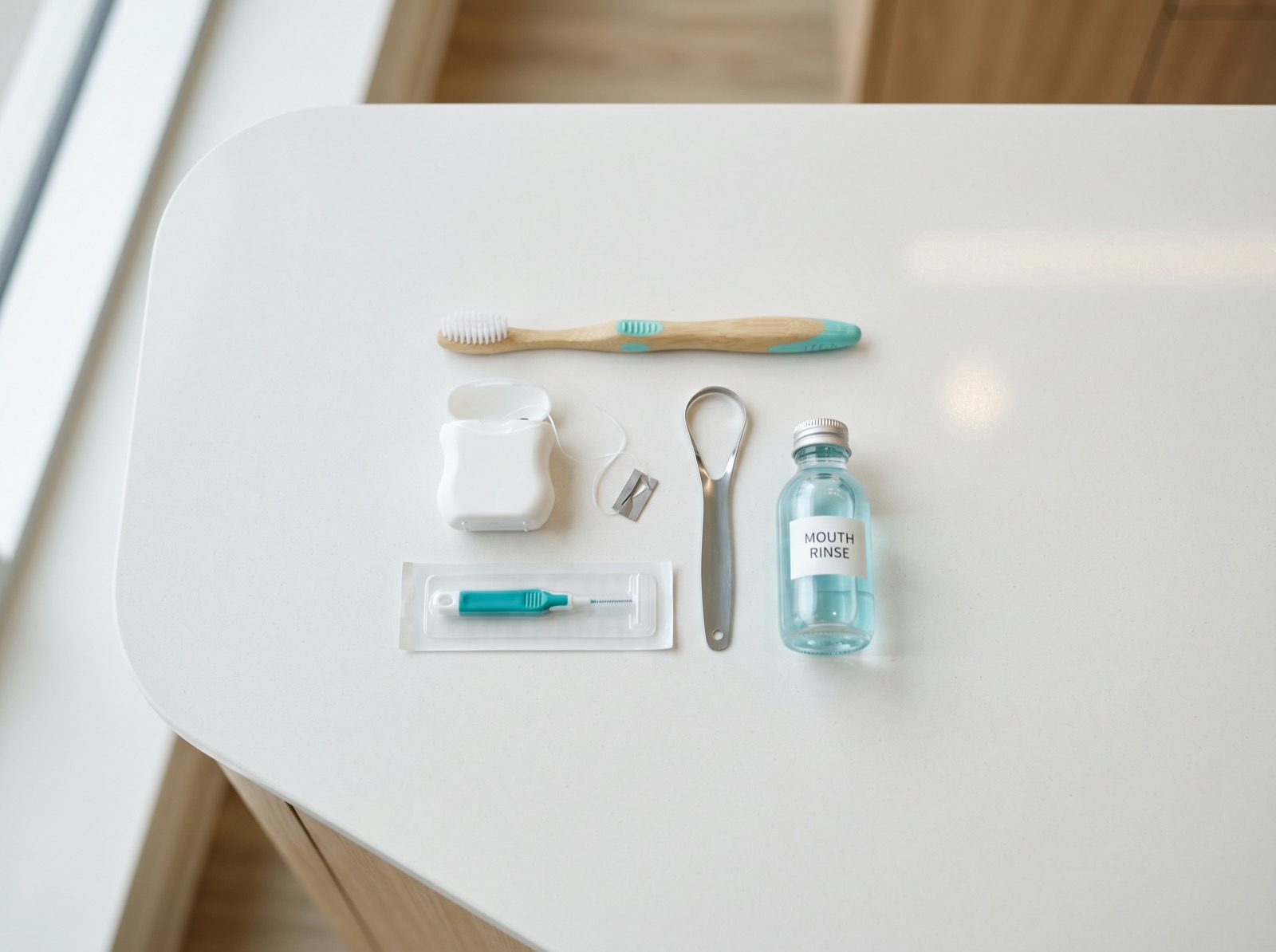 A neat top-down flat-lay of a toothbrush, dental floss, interdental brushes, a tongue cleaner and mouth rinse