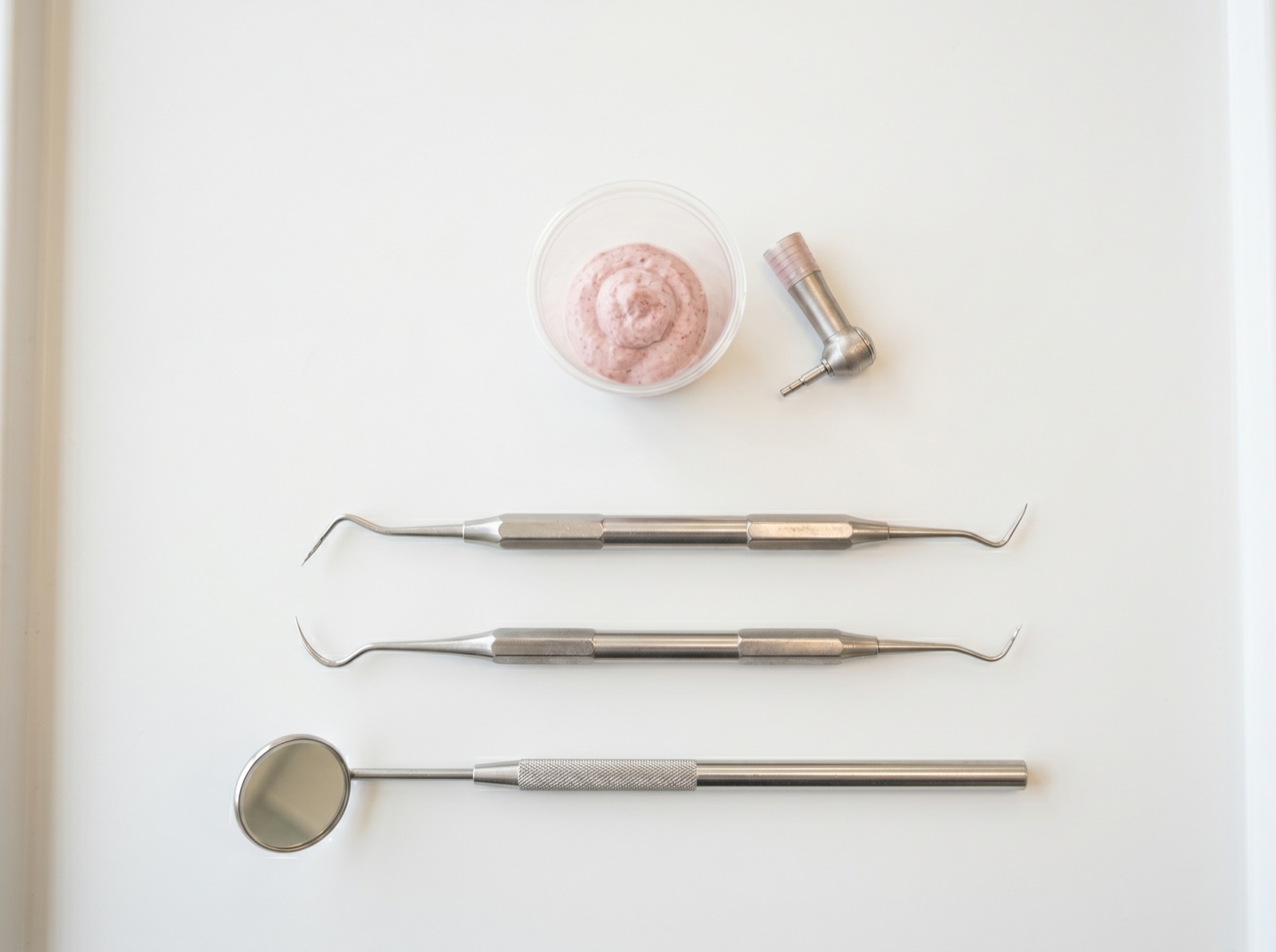 A flat-lay of dental cleaning instruments — an ultrasonic scaler, hand scaler and mirror — on a clean tray
